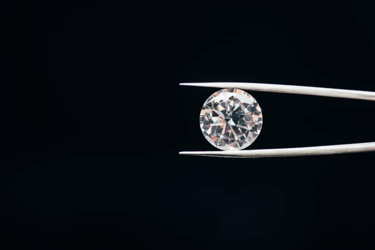 diamond held by tweezers in front of dark background