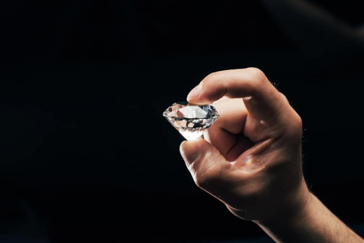 diamond held by hand in front of dark background