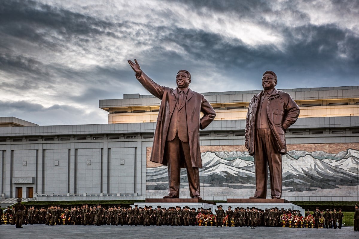 Military lined up under a large bronze statue in North Korea by Tariq Zaidi