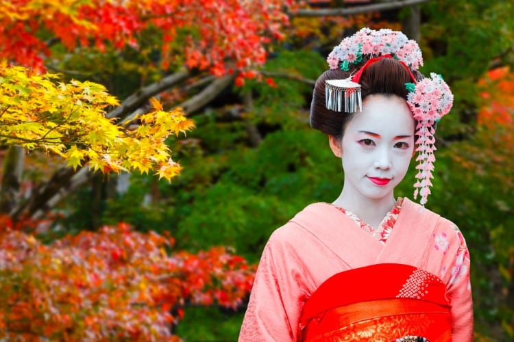 Maiko in Japan in front of a tree with colorful foliage