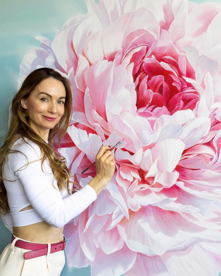 Artist Ira Volkova Standing Next To Her Detailed Painting Of A Pink Peony
