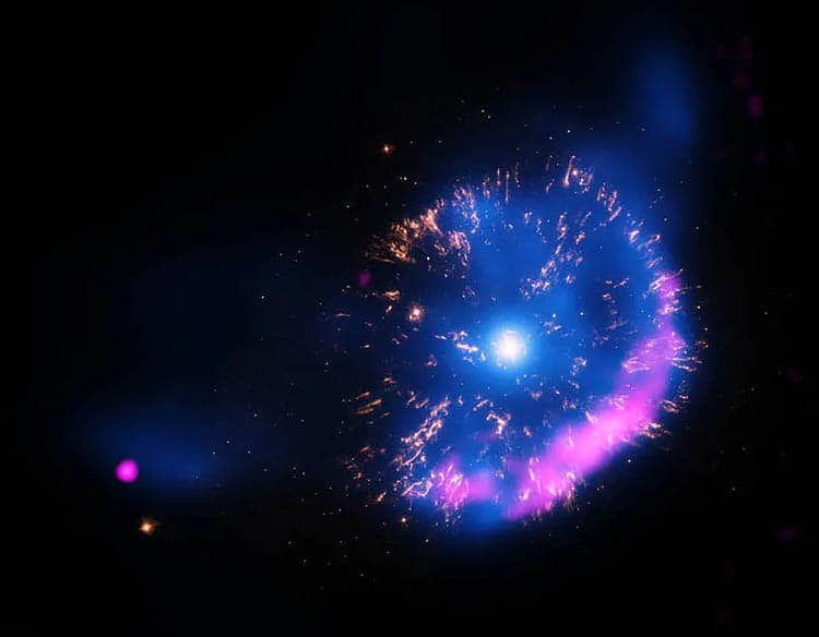 This new image of GK Persei contains X-rays from Chandra (blue), optical data from NASA’s Hubble Space Telescope (yellow), and radio data from the National Science Foundation’s Very Large Array (pink). The X-ray data show hot gas and the radio data show emission from electrons that have been accelerated to high energies by the nova shock wave. The optical data reveal clumps of material that were ejected in the explosion. The nature of the point-like source on the lower left is unknown.