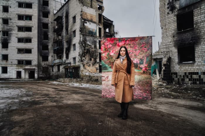 Woman in Ukraine posing in front of flower background with bombed buildings in the back