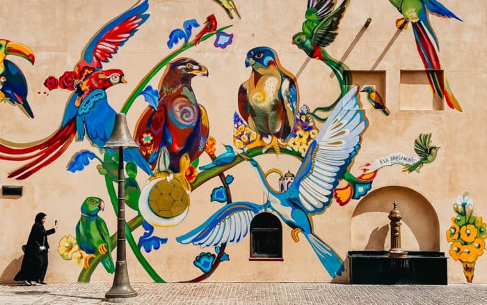 Woman walking in front of colorful mural of birds
