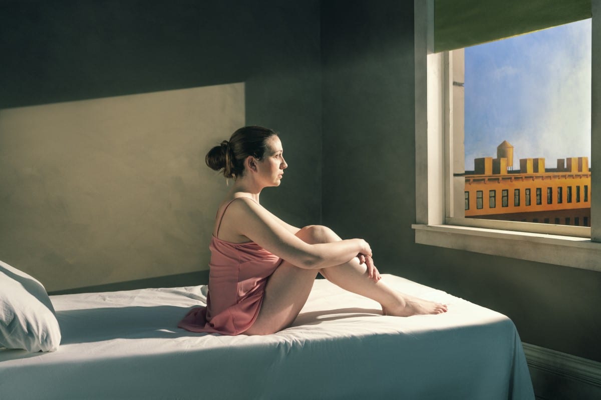 Photo of a woman sitting on a bed looking out a window