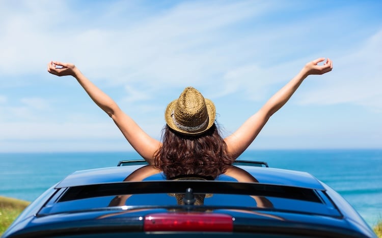 Woman poking out of the top of a car with her hands stretched out in joy