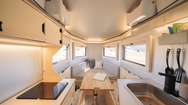 Interior Shot Of Camper Showing Beds, Table, And Kitchen Set Up