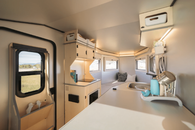 Interior Shot Of Camper Showing Beds, Table, And Kitchen Set Up