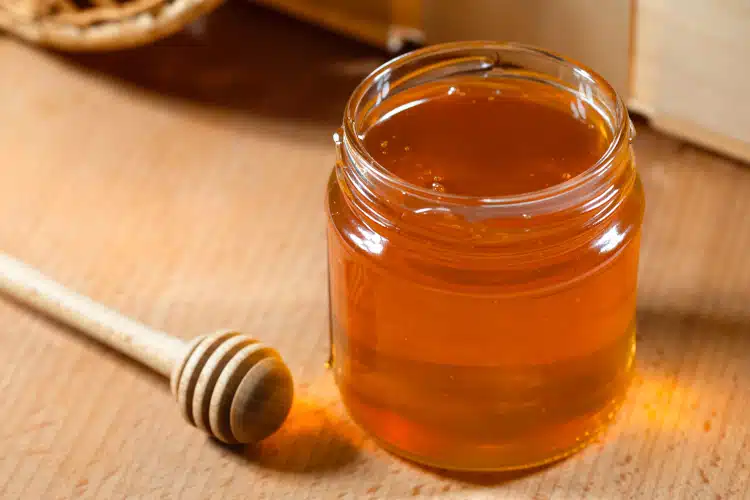 A jar of fresh honey and a honey ladle on a wooden table.