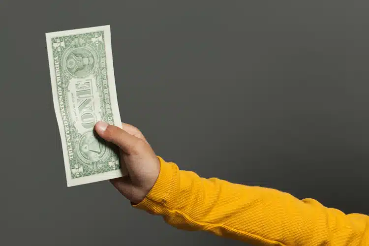 Dollar bill held by the hand of a black boy.