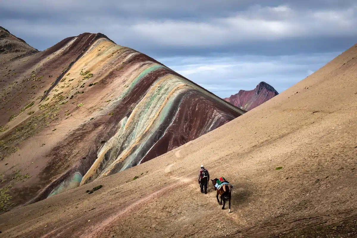 Local horse rider walking towards an amazing 5,000-meter mountain pass next to a Rainbow Mountain in the highlands of the Peruvian Andes.