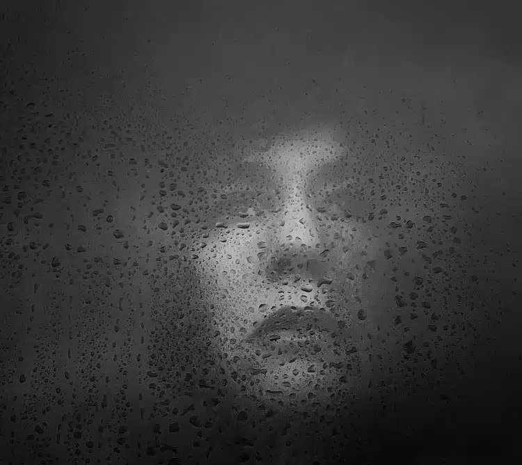 Black and white portrait of a woman behind a wet window