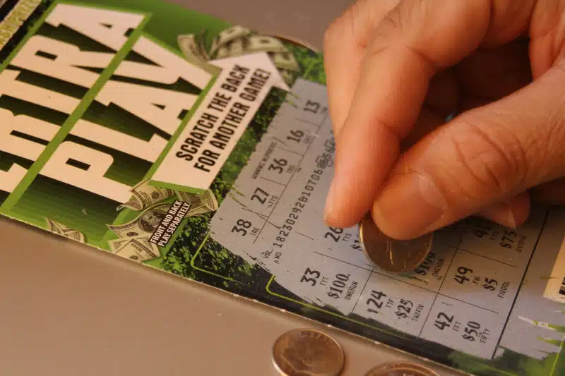 Person's hand scratching off ticket with a coin