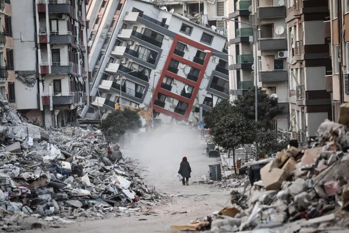 Following the powerful February 2023 earthquake in Hatay, Turkey, a woman walks past a collapsed building as demolition teams work nearby