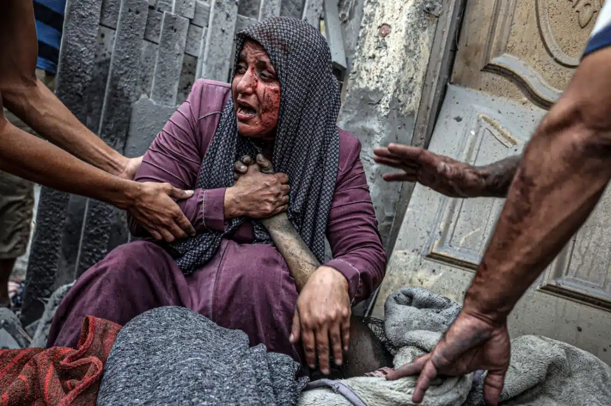 Amidst the chaos and devastation left by an Israeli airstrikes in the Ridwan neighborhood of Gaza City, an injured woman is overcome with grief beside the lifeless body of a loved one.