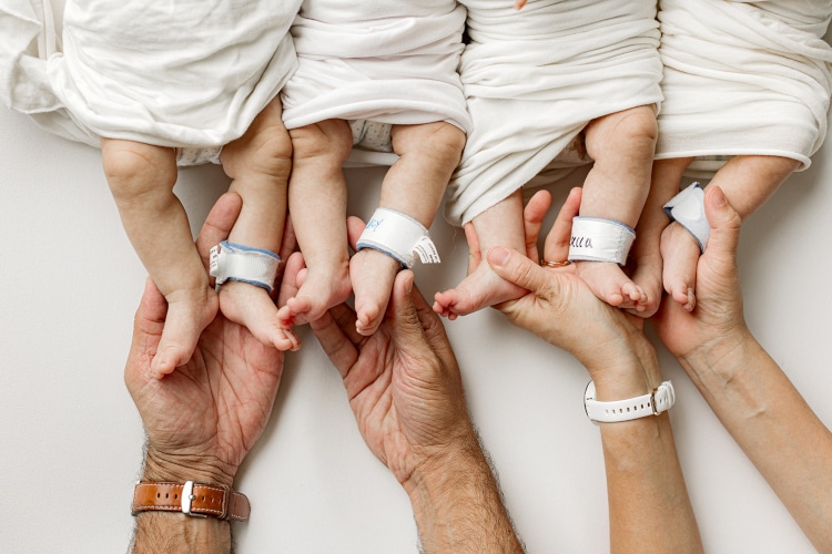 Adult hands holding the feet of baby quadruplets 