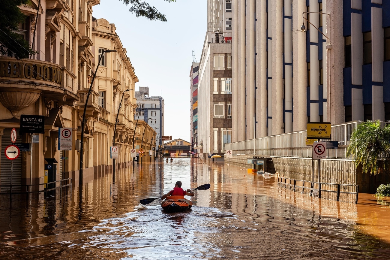 Young man rowing kayak through floodwaters in Porto Alegre, Brazil, during the devastating Rio Grande do Sul floods in Spring 2024