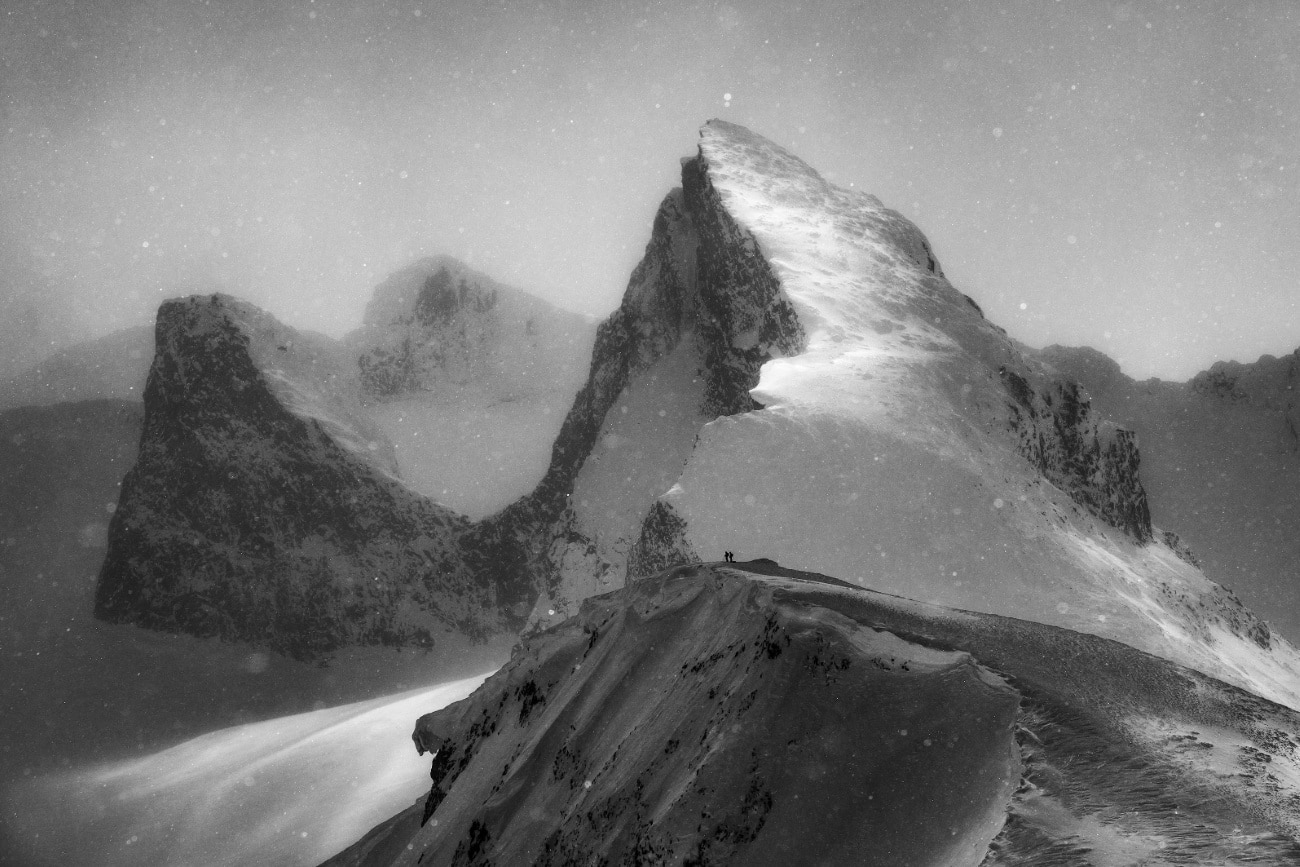 Store Smørstabbtinden mountain in Norway’s Jotunheimen National Park, light snow falls as two skiers watch over a sublime winter landscape.