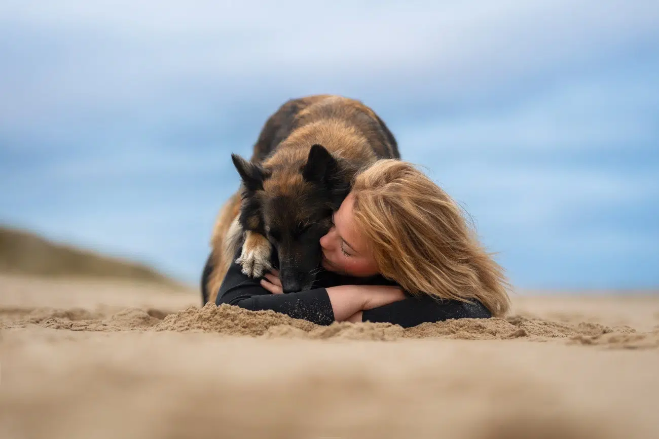 Woman and dog snuggling on the beach
