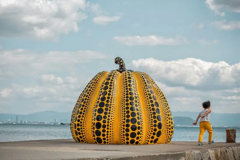 One of Yayoi Kusama's pumpkin sculptures at a pier with a child running beside it