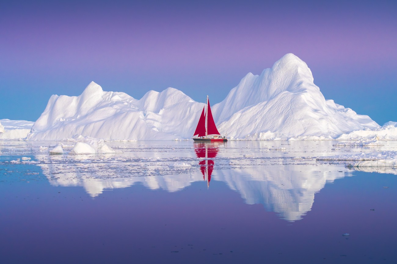 Albert Dros red sailboat in Disco Bay with an iceberg behind it