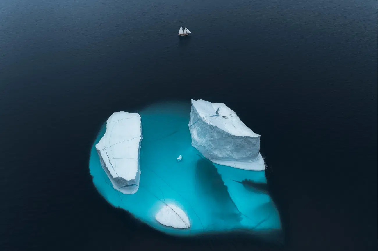 An aerial view of two massive icebergs floating in deep blue Arctic waters deep within Greenland's massive fjords