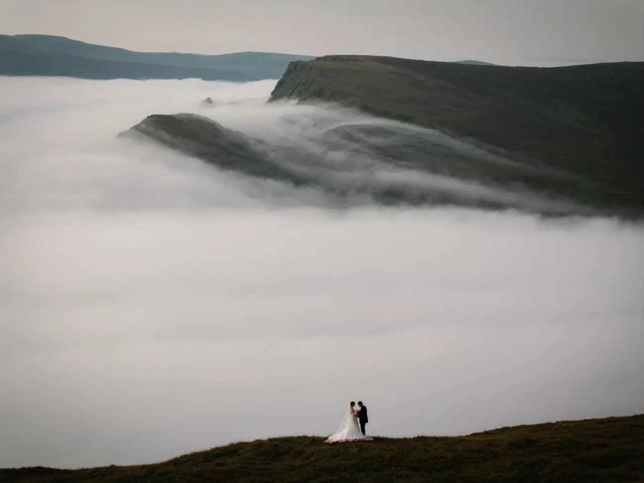 A newlywed couple stands above the clouds after hiking up a hill on the Isle of Skye, Scotland.