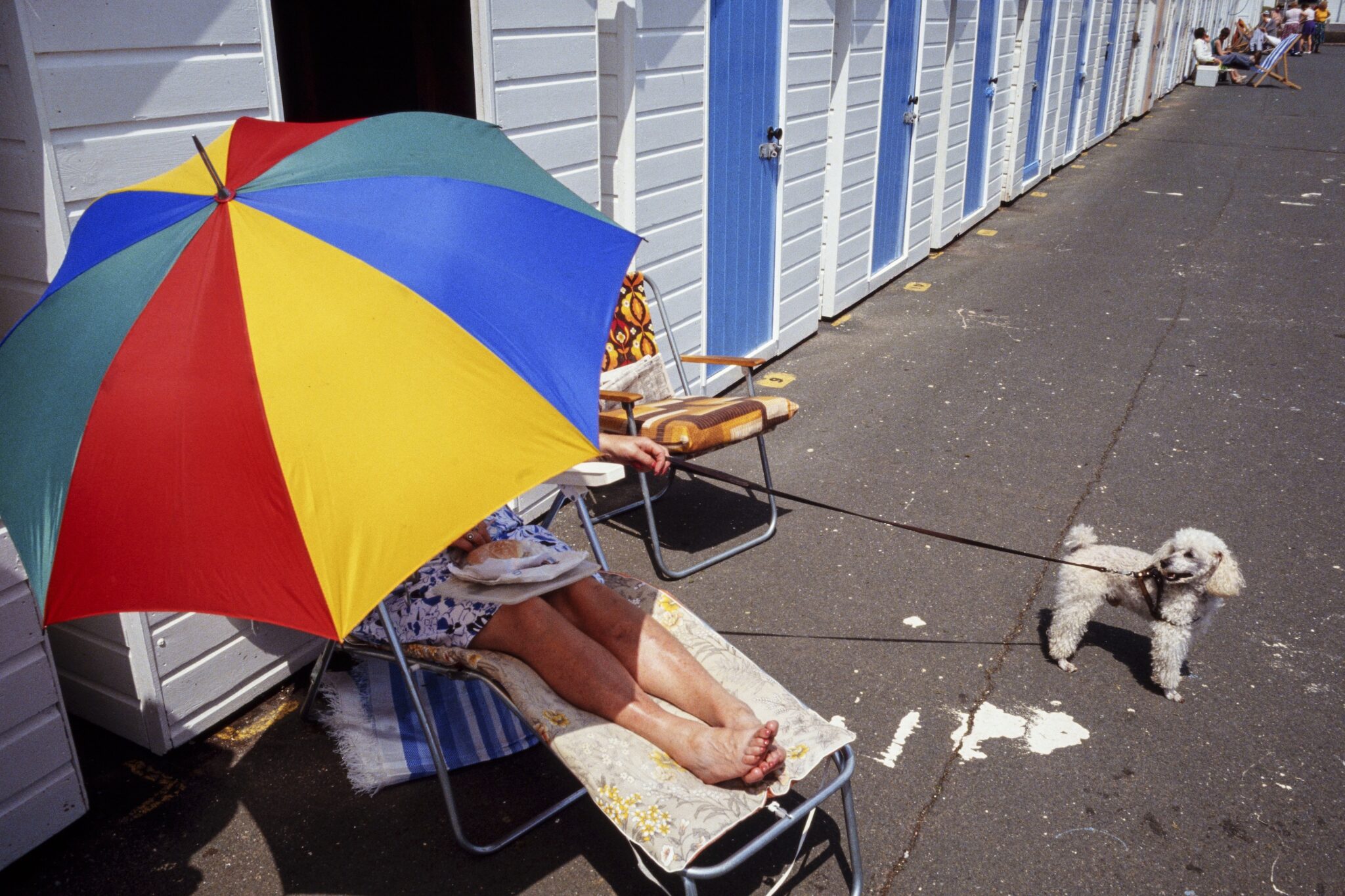 Richard Baker, 1993. Shaded from the mid-day sun, a holidaymaker holds on to her pet poodle on Paignton seafront, England. Out of financial necessity, thousands of British vacationers returned to the beaches of their youths rather than taking package trips to Mediterranean resorts.