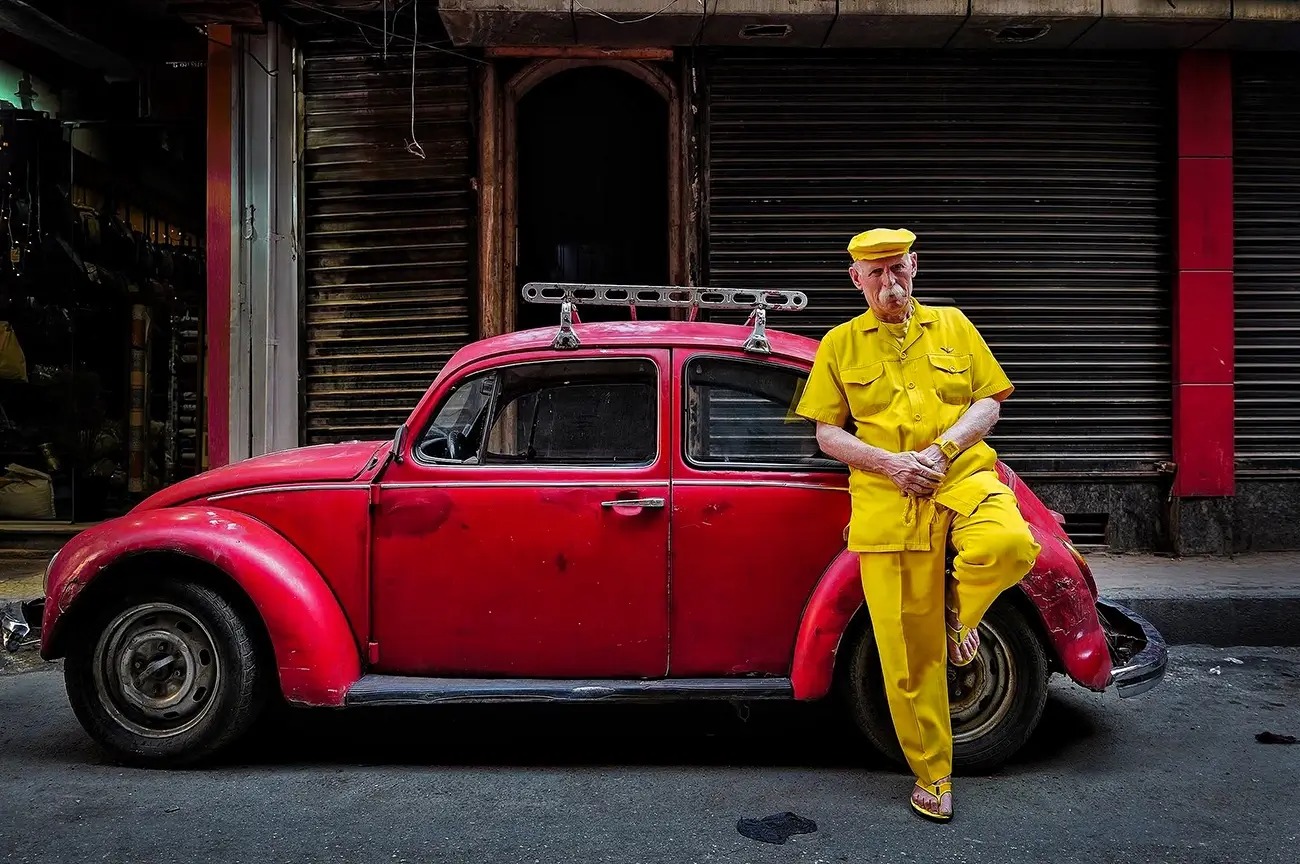 Man dressed in yellow in Aleppo leaning against a red car