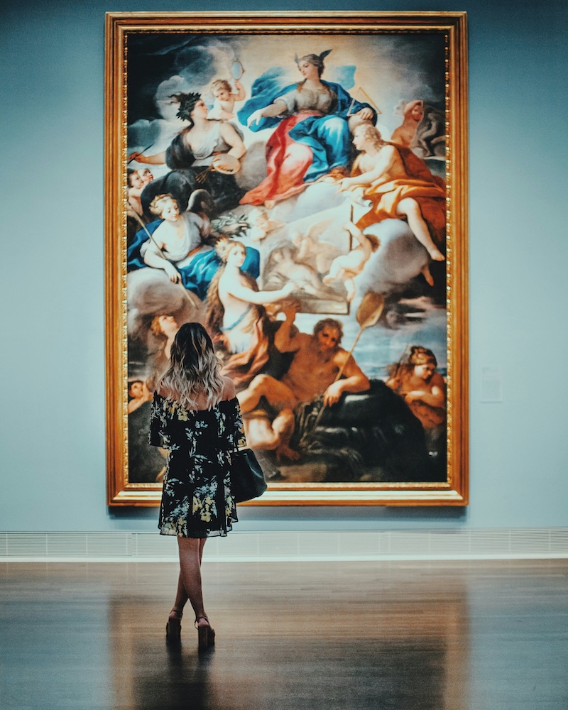 Woman at an art gallery looking at a very large painting on a wall