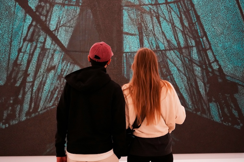 A man and a woman with their backs turned to the viewer, looking at a large piece of art