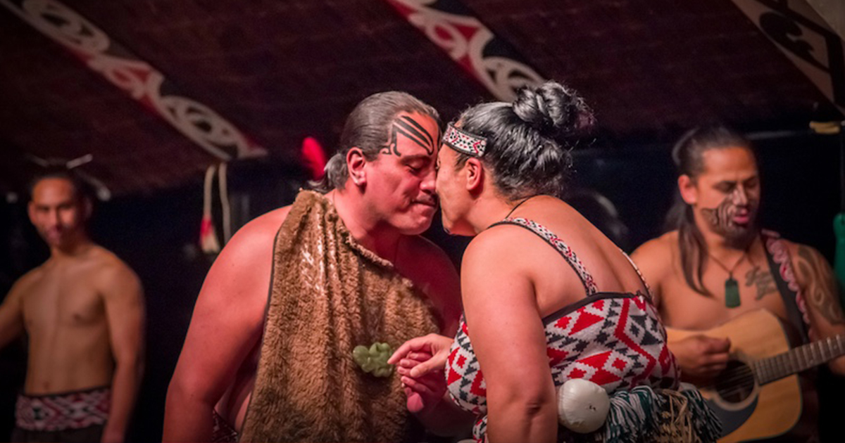 An intimate, artistic close-up photograph showing two human hands with intricate traditional Māori tā moko (tattoo) patterns covering the skin in black ink. The traditional geometric and spiral designs include curved lines, dots, and angular patterns that are characteristic of Māori cultural body art. The hands appear to belong to someone wearing dark clothing, though only the hands and lower sleeves are visible in the frame. The photograph is taken against a neutral background, emphasizing the detailed craftsmanship and cultural significance of the tā moko. These traditional tattoos represent Māori identity, genealogy, and cultural connection, which relates to the article's discussion of how Māori language and culture offer a respectful, non-pathologizing approach to understanding autism through the word Takiwātanga - meaning 'in one's own time and space.' The image symbolizes the deep cultural wisdom and inclusive perspective that Indigenous communities bring to understanding neurodiversity.