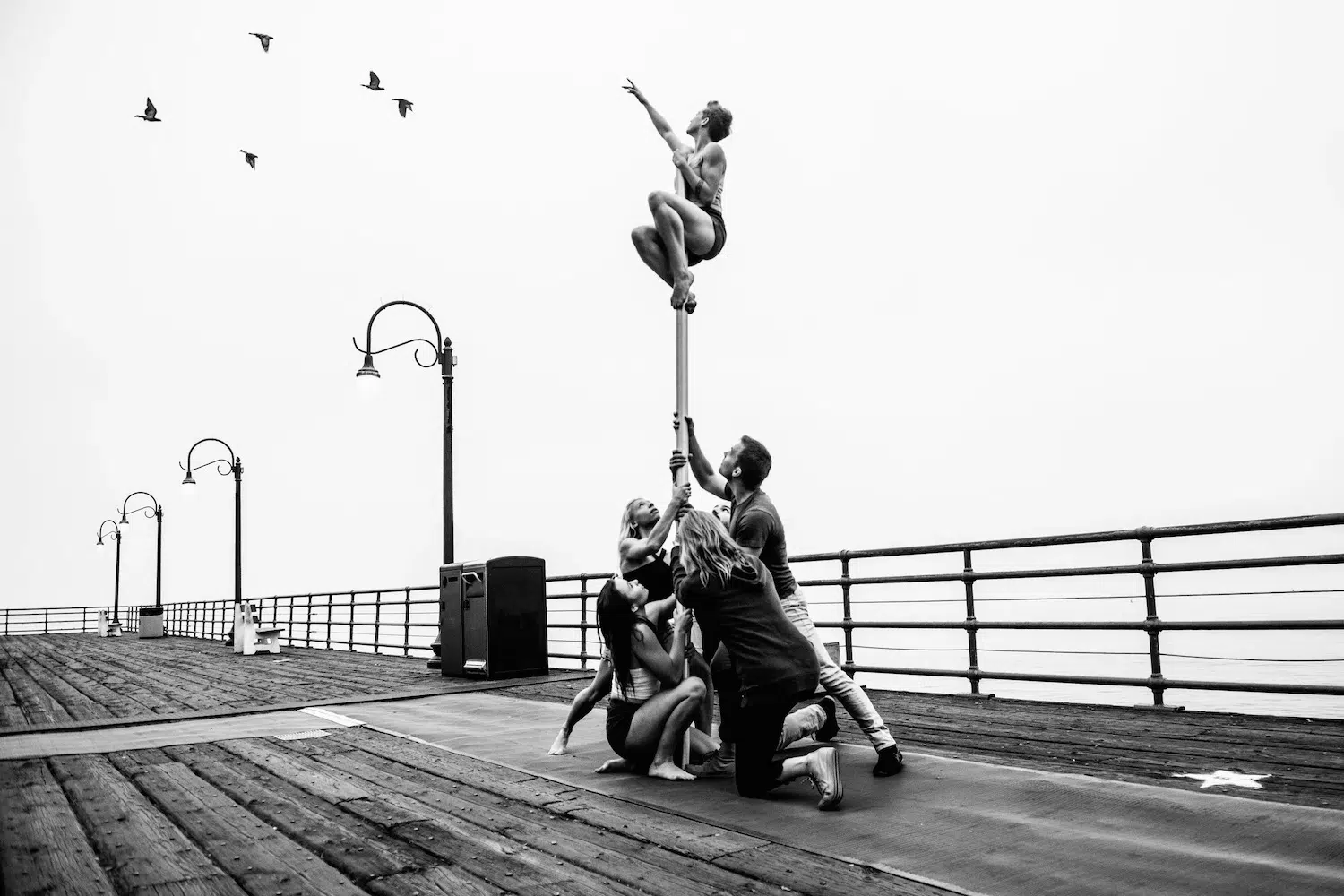 Dance photograph captured by Josh S. Rose, featuring a group of dancers holding up a stick, upon which a man is perched