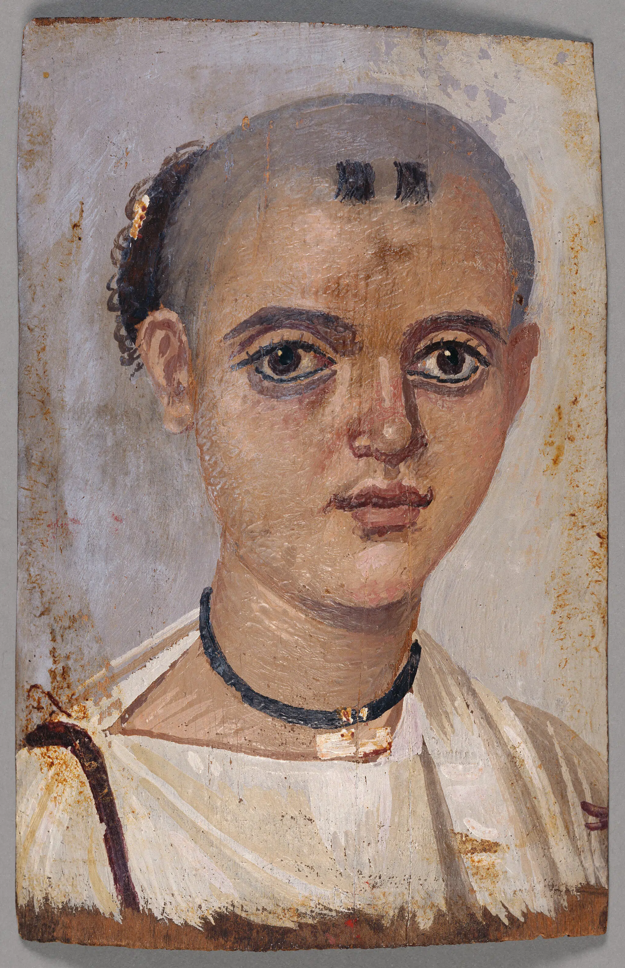 Mummy portrait of a youth wearing an amulet. Egyptian, 150-200 CE. Encaustic on linden wood.
