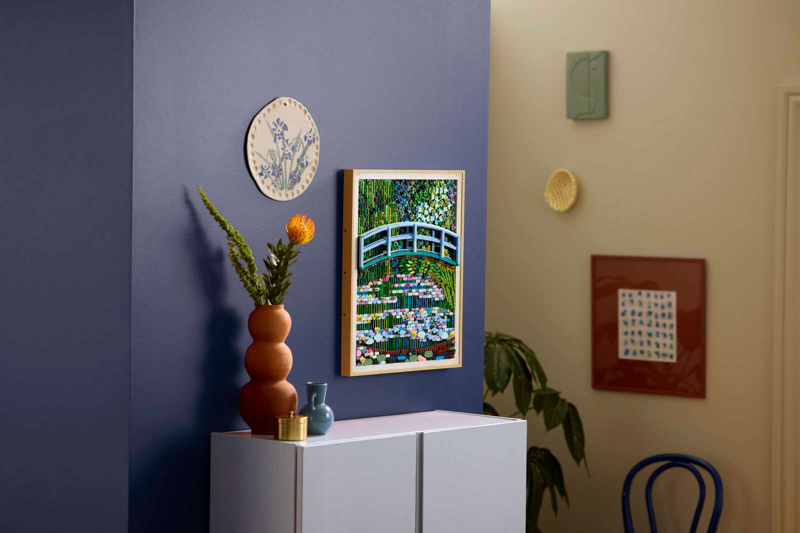 The &lsquo;Monet Bridge Over a Pond of Water Lilies&rsquo; LEGO set hanging on a purple wall above a cabinet