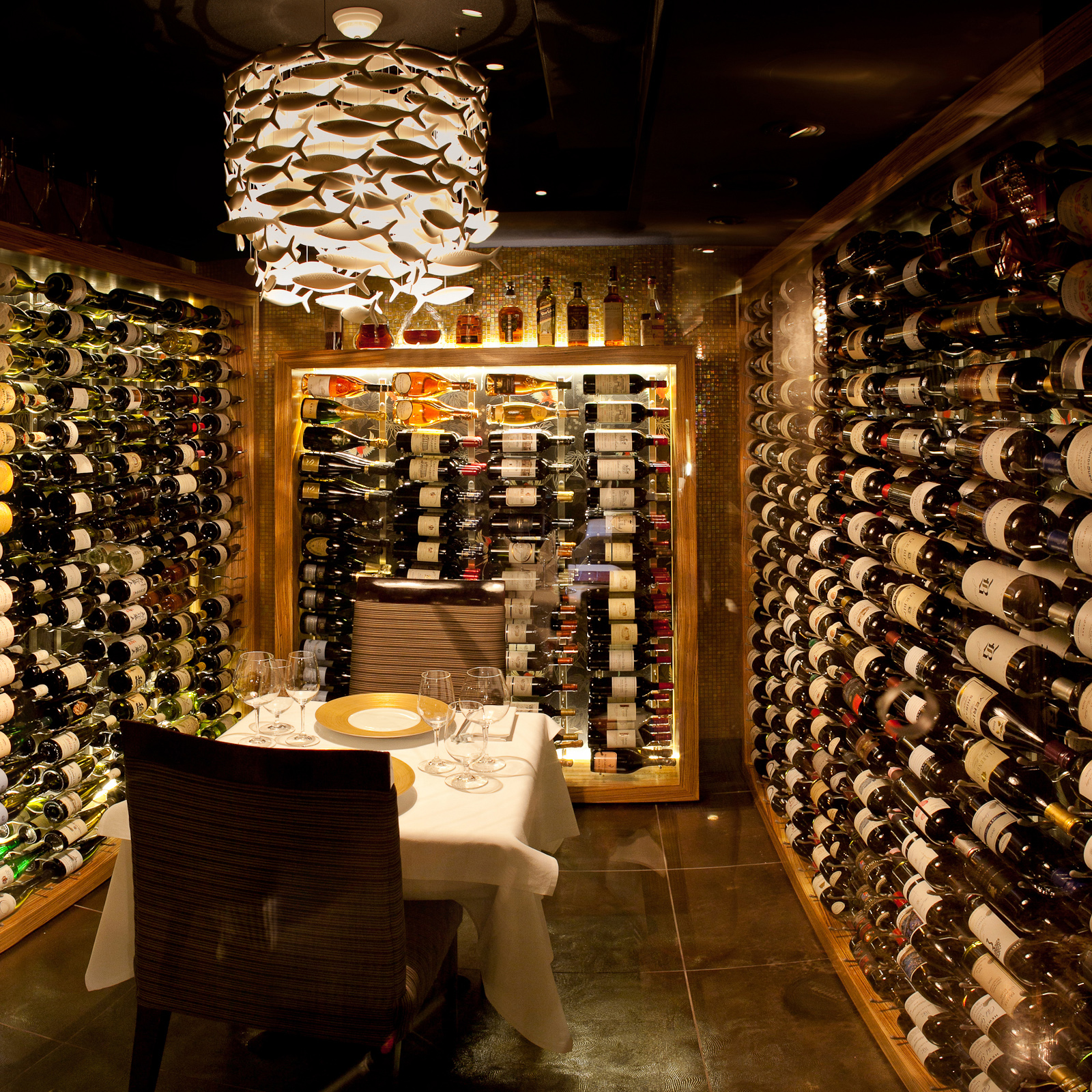 A Scabetti chandelier composed of ceramic fish hanging above a dining table in a wine cellar