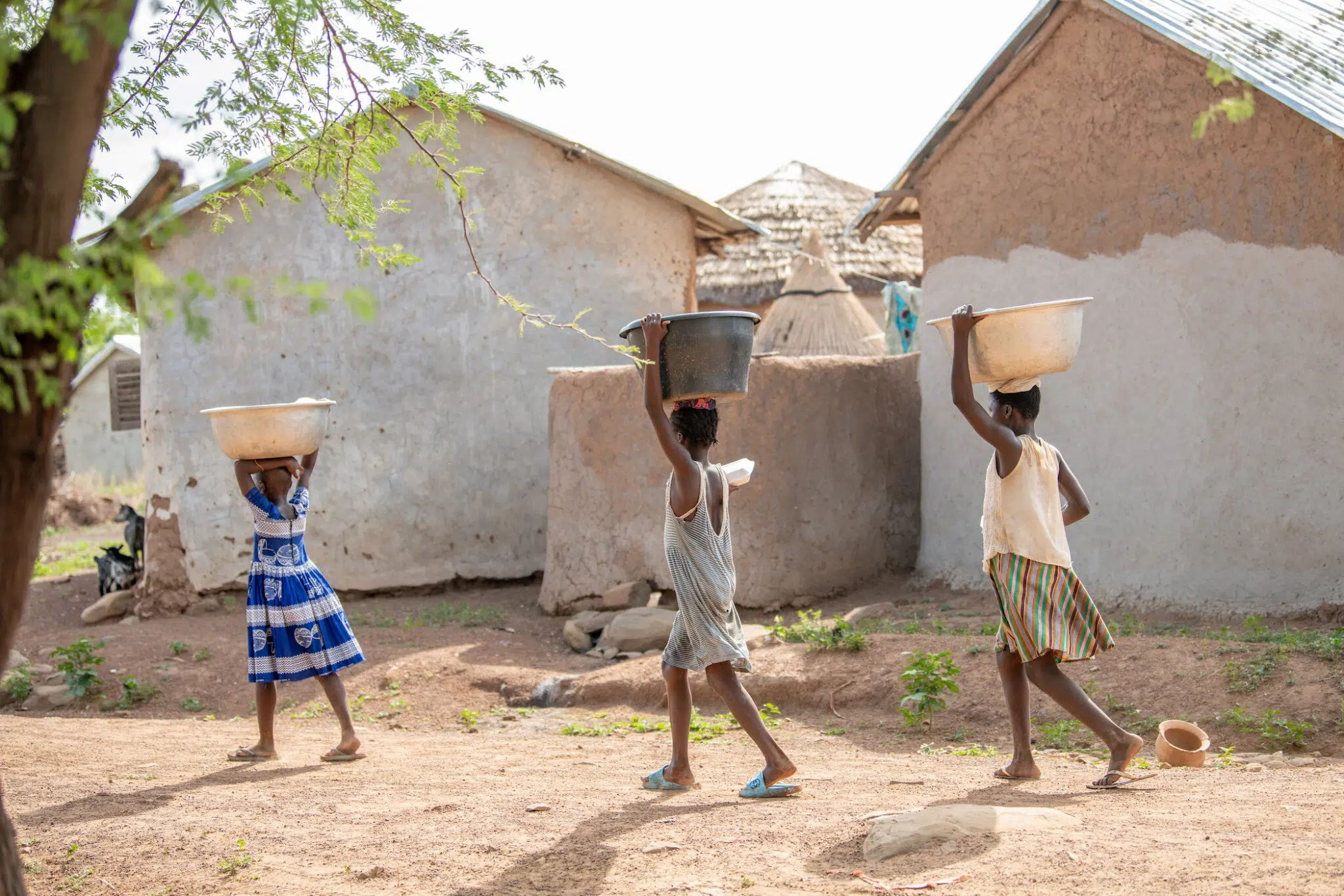 Ghana, May 11, 2025. Children carry water from the communal pump at the Gnani camp for women accused of witchcraft in northern Ghana.