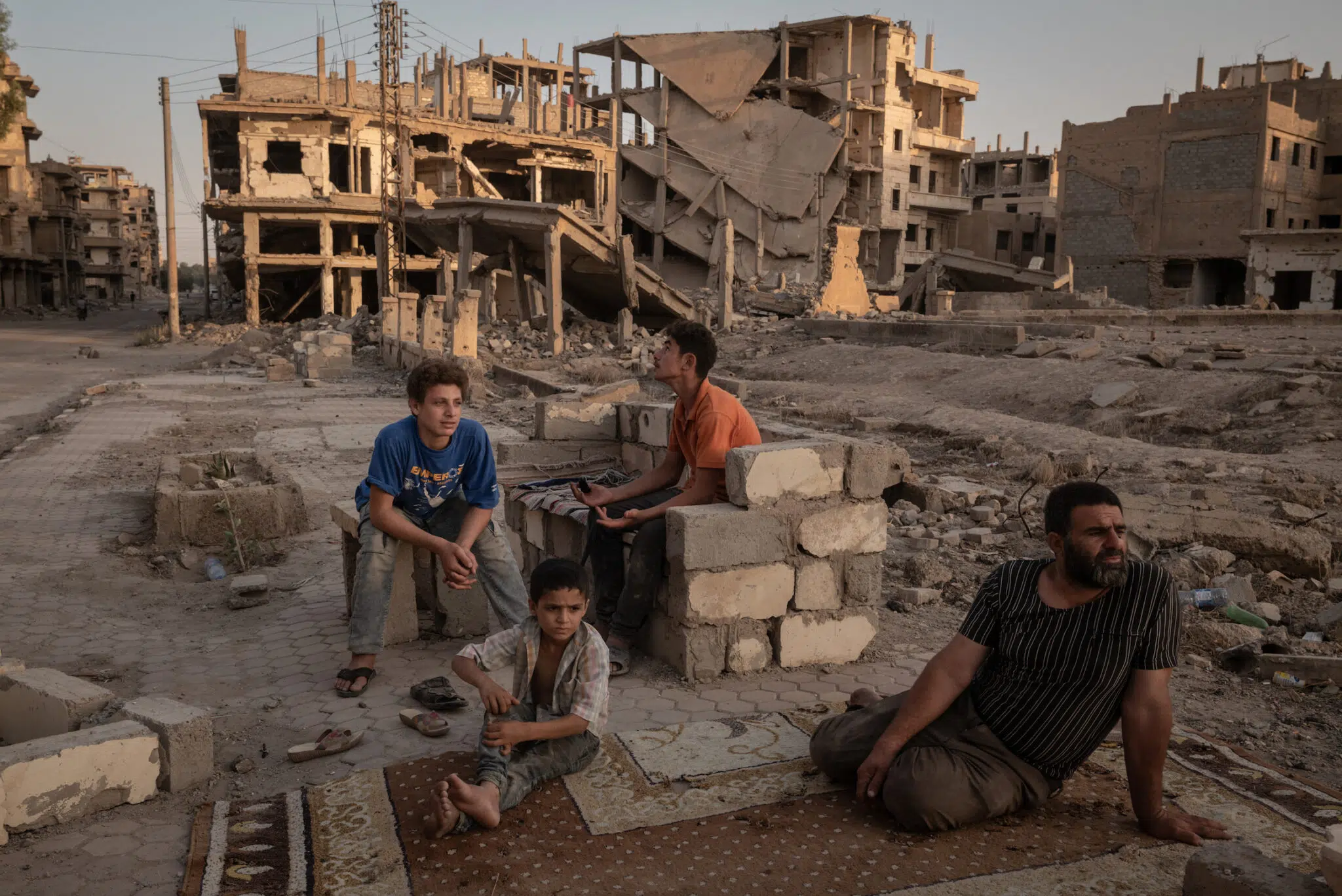 Nicole Tung, &ldquo;A Syrian City Rebuilds, Still Divided,&rdquo; for the New York Times. Abdelatif Daham Al Hummada (r.) sits with his sons and nephew on the street outside their heavily damaged home, where the family often sleeps. Deir al-Zour, Syria, August 20, 2025.