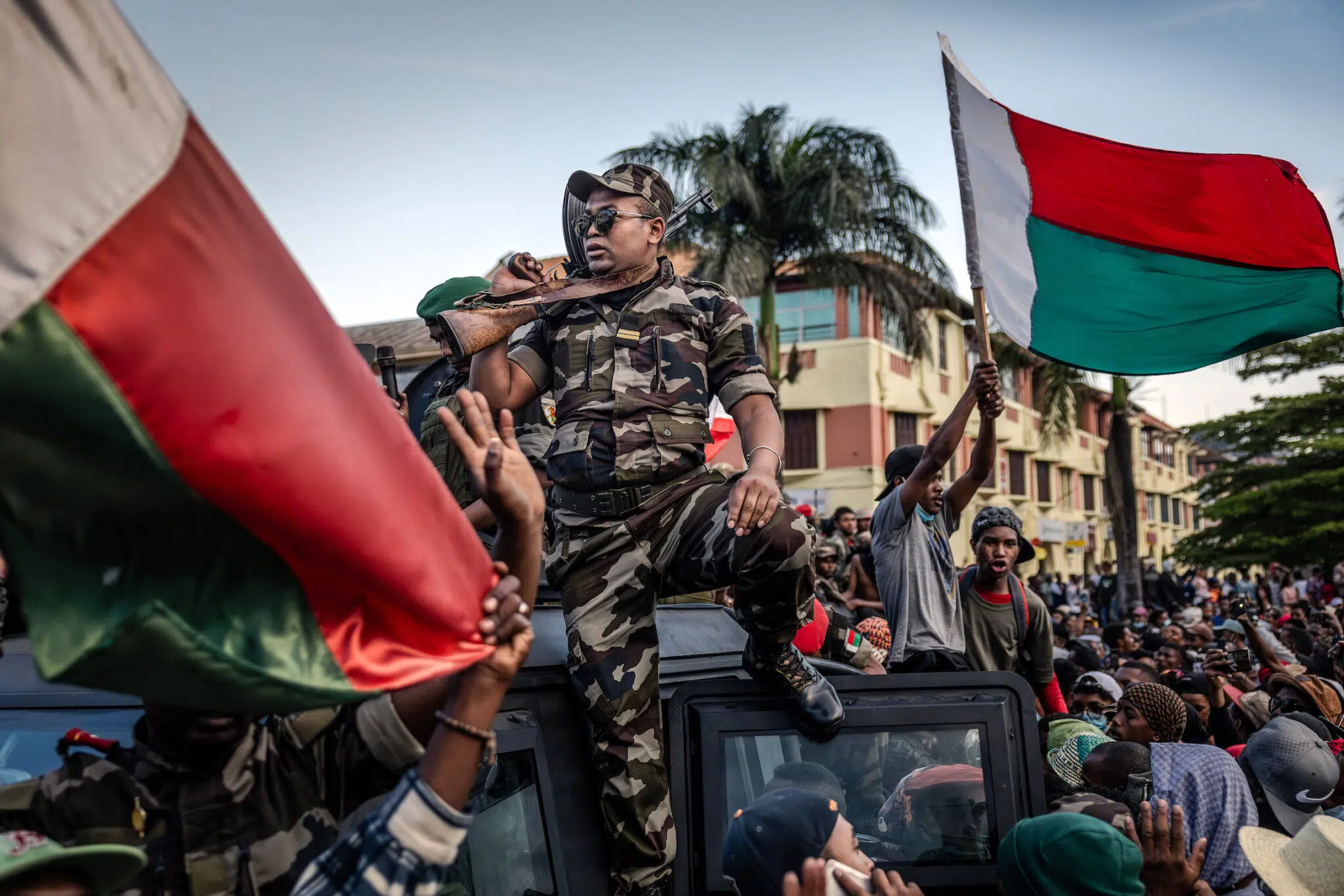 Luis Tato, &ldquo;Madagascar&rsquo;s Gen Z Protests,&rdquo; for Agence France-Presse. Protesters cheer and wave flags outside City Hall as members of the CAPSAT military unit ride on an armored vehicle. Antananarivo, Madagascar, October 11, 2025.