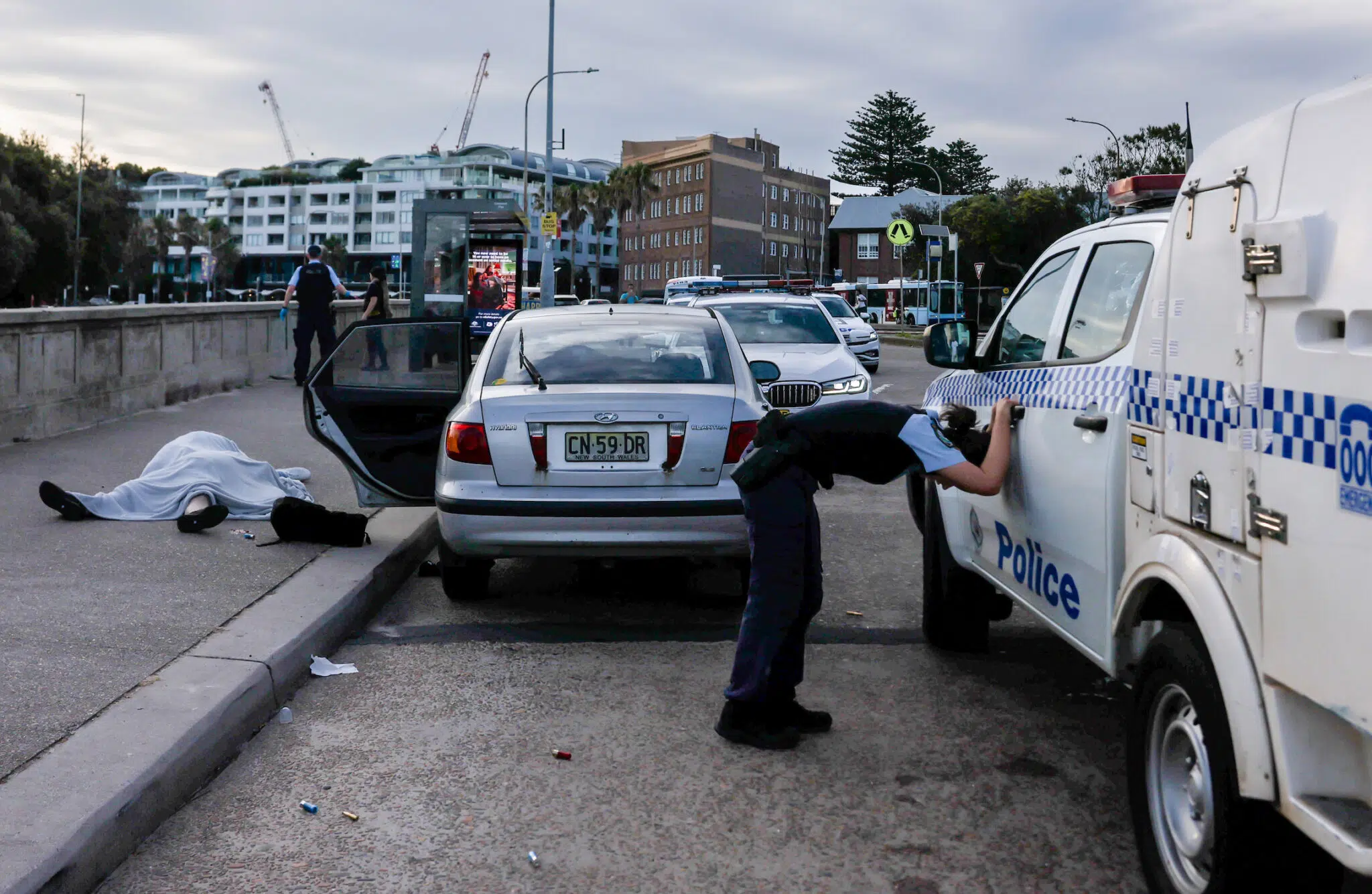Edwina Pickles, &ldquo;Bondi Beach Terror Attack,&rdquo; for the Sydney Morning Herald. An overwhelmed police officer leans over near the bodies of Boris (69) and Sofia (61) Gurman. During the Bondi Beach Terror Attack, the couple were killed while attempting to disarm one of the shooters. Sydney, Australia, December 14, 2025.
