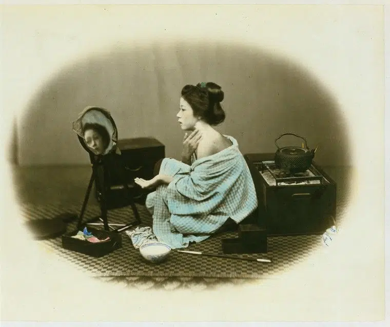 Hand-colored photograph of a woman using cosmetics in 19th-century Japan