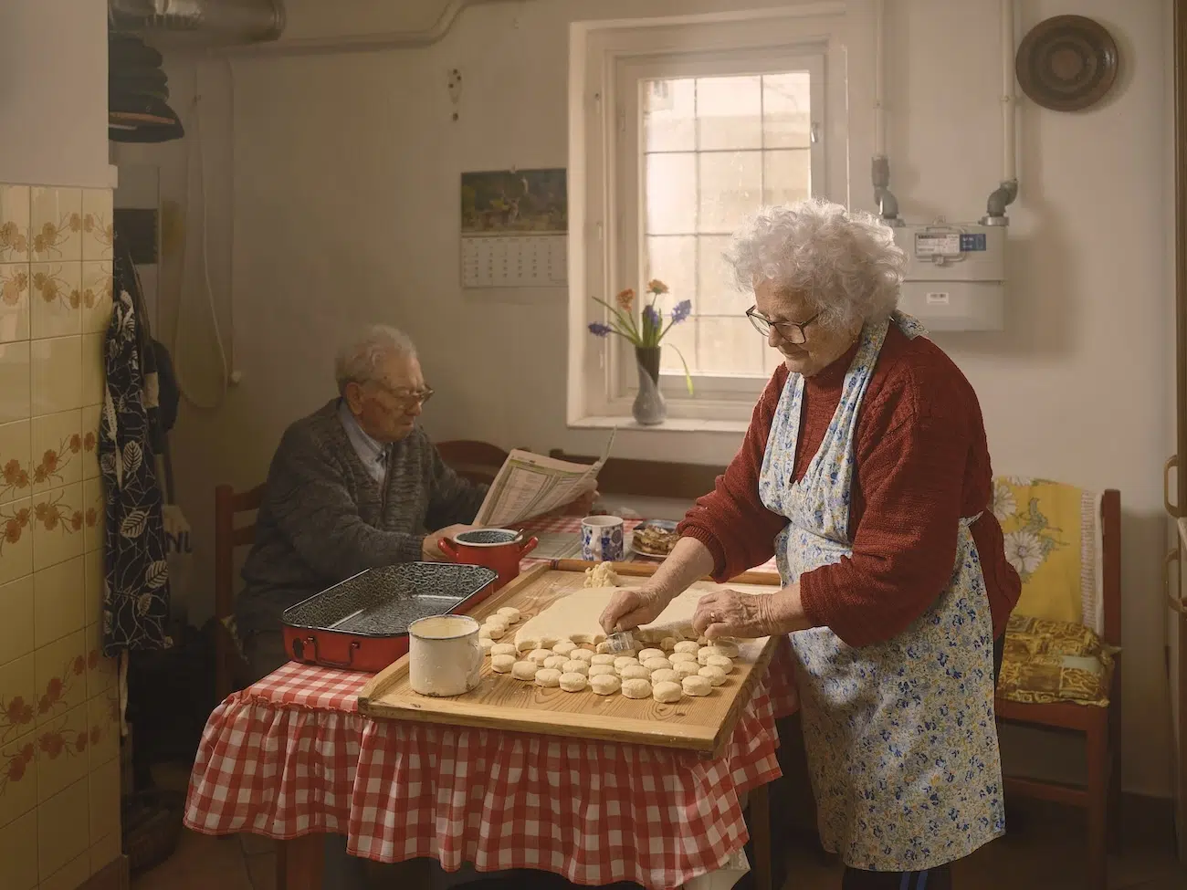 Woman cutting biscuit while man reads newspaper at table