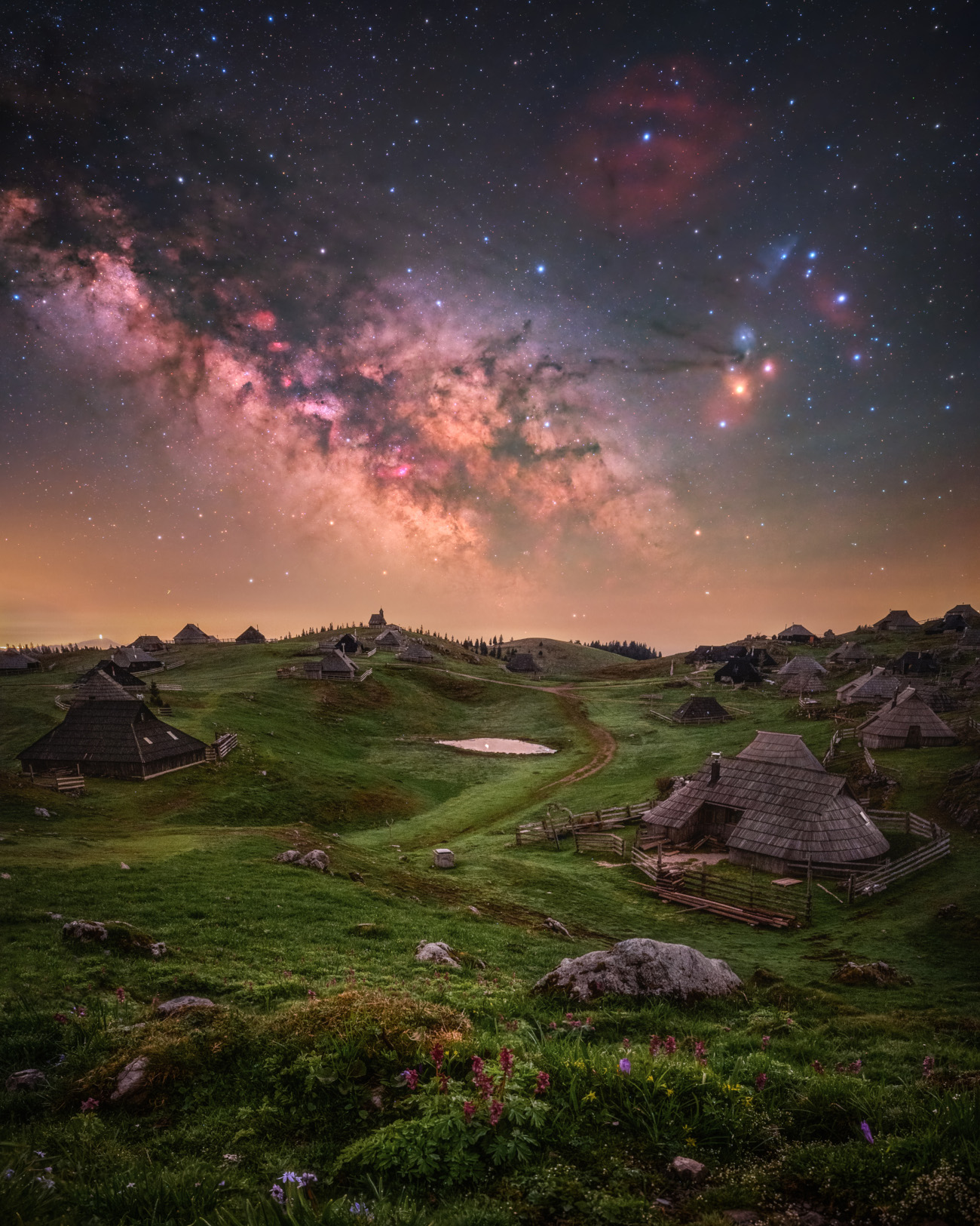 People & Space. "Fairyland" © Uroš Fink (Slovenia). Velika Planina is one of the most beautiful places in Slovenia. In the foreground of this image, a settlement with the wooden huts characteristic of the area can be seen, while in the background the core of the Milky Way rises in all its beauty. Taken with an astro-modified Nikon Z 6II camera, Move Shoot Move Nomad star tracker, 20 mm, Foreground: f/2.0, ISO 1600, 8 x 60-second focus-stacked exposures; Sky: f/2.0, ISO 800, 5 x 60-second exposures. Location: Velika Planina, Kamnik-Savinja Alps, Slovenia, 28
