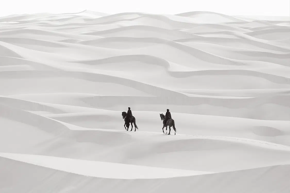 Photo of two figures on horses in the desert.