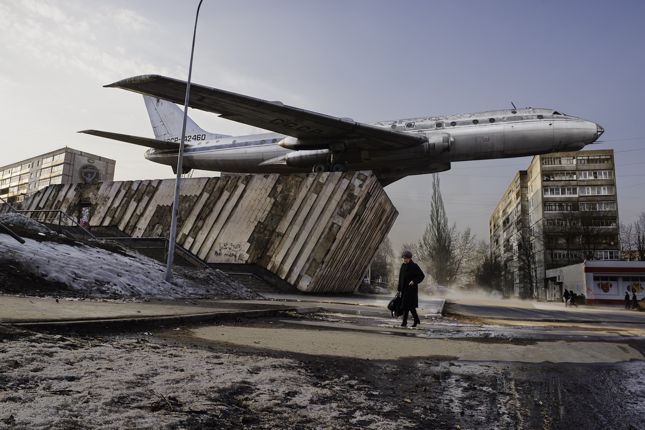 Man in street walking beneath airplane.