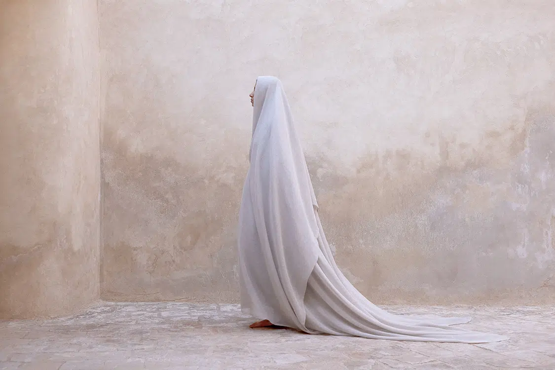Photo of person in flowing fabric against blank wall.