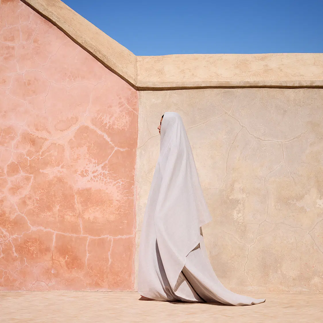 Photo of figure in white cloth in front of wall.