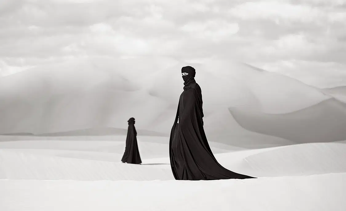 Photo of two figures dressed in black in the desert.