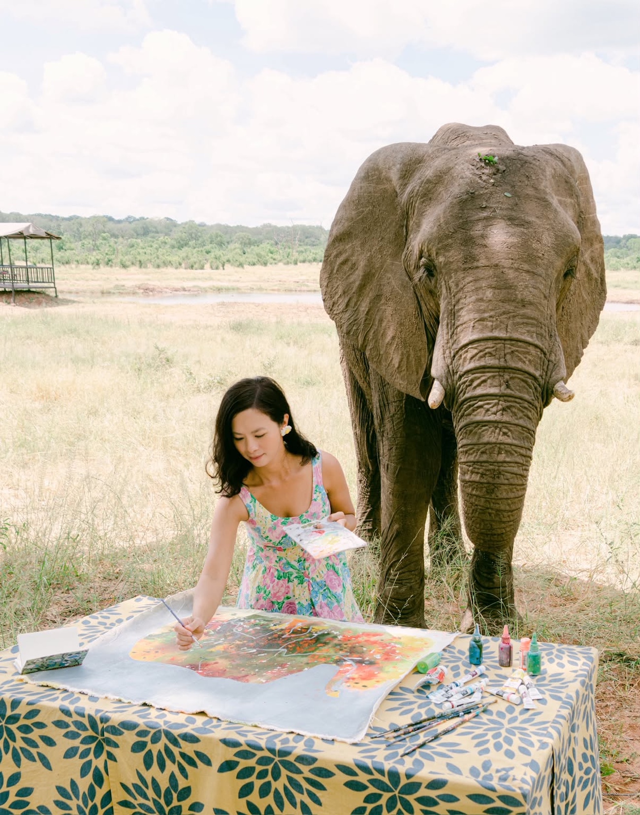 Photo of a woman painting next to an elephant. 
