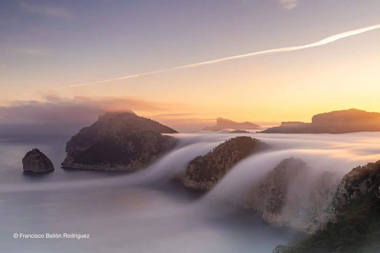 Photo of mist flowing over mountains and into the sea. 